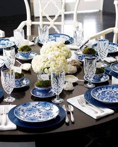 a table set with blue and white plates, silverware and flowers in vases