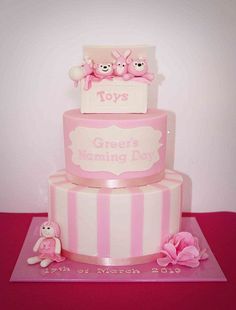 a three tiered cake with pink and white stripes on the bottom, topped with two teddy bears