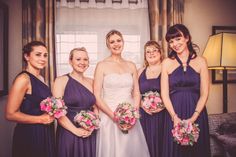 a group of women standing next to each other in front of a window holding bouquets