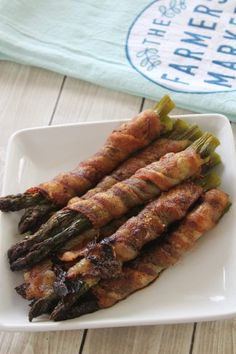 asparagus wrapped in bacon on a white plate next to a towel and napkin