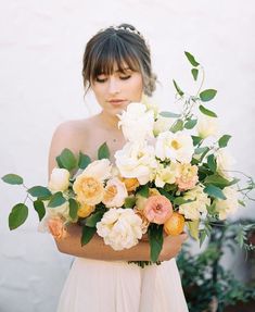 a woman holding a bouquet of white and peach flowers in her hands with greenery around her neck