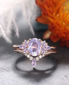 an engagement ring with three pear shaped pink sapphires and diamonds on the side, surrounded by feathers