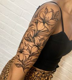 a woman's arm with flowers and leaves tattooed on her left arm, in front of a white brick wall