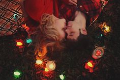 a man and woman laying on the ground surrounded by christmas lights with their faces close to each other