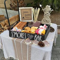 a table topped with lots of different types of food and desserts next to a sign that says s'mores bar