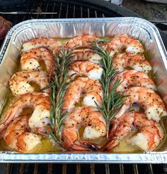 cooked shrimp with rosemary on top in an aluminum baking pan, cooking over an open grill