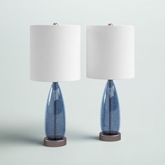 two blue glass table lamps with white shades on each lamp and one is turned off