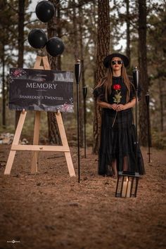 a woman in a black dress and hat standing next to an easel with balloons on it