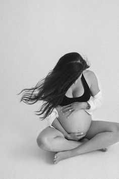 a pregnant woman sitting on the floor with her hair blowing in the wind while holding her belly