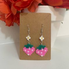 a pair of pink and green earrings with flowers on them sitting in front of a flower pot