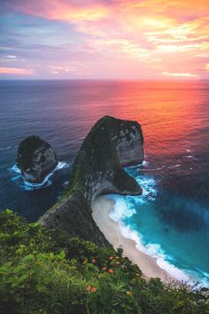 two large rocks sticking out of the ocean next to a sandy beach with blue water