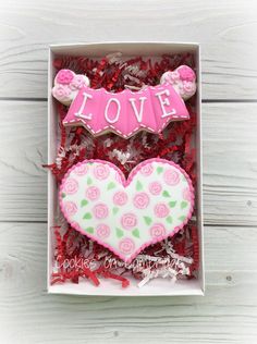 two decorated cookies in a box with the word love spelled on top and roses around it