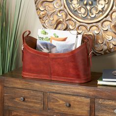 a brown leather purse sitting on top of a wooden dresser next to a plant and books