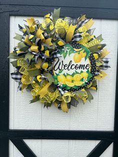 a yellow and black wreath with the words welcome on it hanging on a white door