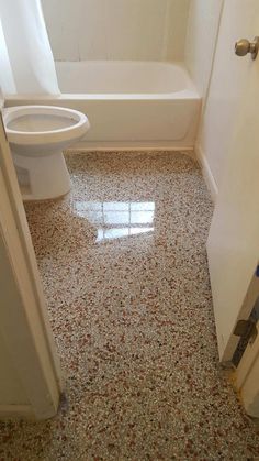 a white toilet sitting next to a bath tub in a bathroom on top of a tiled floor