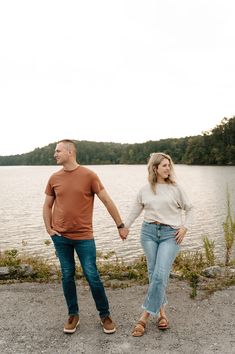 a man and woman standing next to each other holding hands by the water's edge