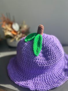 a crocheted purple hat with a green leaf on the brim sits on a table