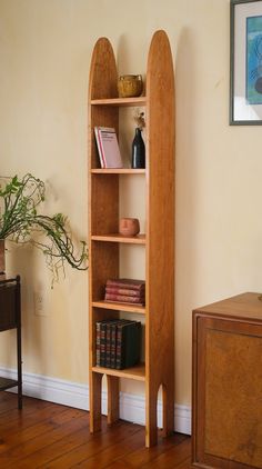 a tall wooden book shelf with books on top of it next to a plant in a vase