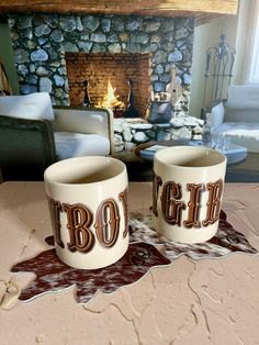 two coffee mugs sitting on top of a table in front of a fire place