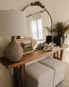 a table with a mirror, vases and other items on it next to a lamp