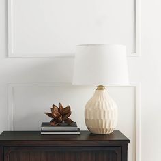 a white vase sitting on top of a wooden table next to a book and lamp