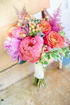 a bouquet of pink flowers sitting on top of a wooden bench next to a chair