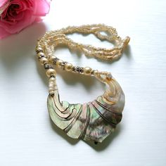 This necklace is from Bali and it is wonderful. A fair trade product of our Balinese partner, Nyoman, it comprises ceramic beads with beautiful abalone Shell, it is 23 inches long or 59 cms. The pendant catches the light to really highlight its unique fan design. Beads are ceramic. The pendant is 3 inches wide by 1.5 inches high (7.5 cms by 3.75 cms ). The carving and polishing of the abalone shell are very delicate. All our products from Bali were designed by myself and made by our fair trade partners who directly benefit from your orders We are proud to offer it at a very reasonable price as always with us there is no middleman. PLease visit my other esty shop, Rosa Azul Crafts, for Mexican and Guatemalan Fair Trade goods https://www.etsy.com/uk/shop/RosaAzulCrafts Handmade Pearl Beaded Necklaces For Festivals, Handmade Pearl Necklace For Vacation, Handmade Pearl Beaded Necklace For Festivals, Adjustable Polished Bead Necklaces For Beach, Adjustable Polished Beads Necklace For Beach, Bohemian Beach Jewelry With Polished Beads, Bohemian Pearl Necklaces For Jewelry Making, Bohemian Beaded Necklaces For Beach With Polished Beads, Bohemian Polished Beads Jewelry For The Beach