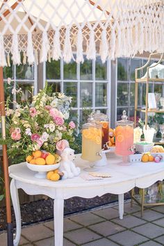 a table topped with lots of fruit and drinks next to a window filled with flowers