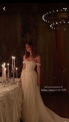 a woman in a white dress standing next to a table with many candles on it