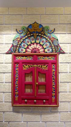 a red cabinet with ornate designs on the front and sides against a white brick wall