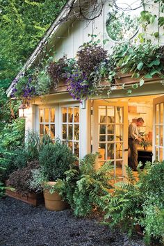 a man standing in the doorway of a house with lots of plants growing on it