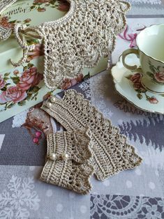 two crocheted mittens are sitting next to a tea cup and saucer