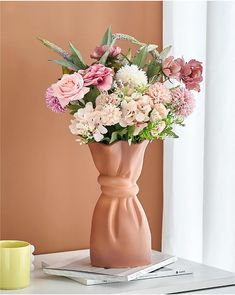 a vase filled with pink and white flowers on top of a table next to a cup