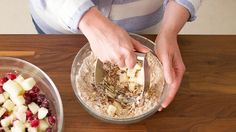 a woman mixing ingredients in a bowl on top of a wooden table