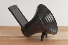 a black speaker sitting on top of a wooden table next to a cell phone holder