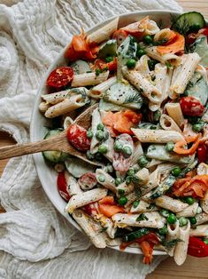 a bowl filled with pasta and vegetables on top of a white cloth next to a wooden spoon