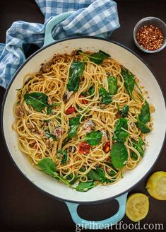 a pan filled with pasta and spinach on top of a table next to sliced lemons