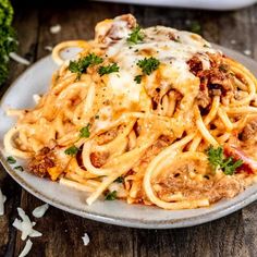 a plate full of pasta with meat and cheese on the table next to some parsley