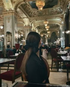 a woman sitting at a table in a fancy restaurant with chandeliers hanging from the ceiling