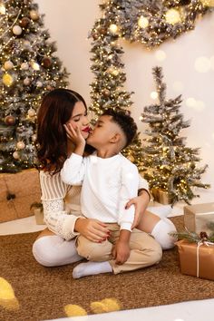 a woman and child sitting on the floor in front of christmas trees