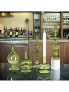 green glass vases and candlesticks on a table in front of a bar