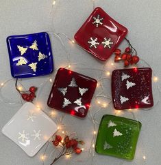 four square glass plates with christmas decorations on them and lights around the edges, all decorated in different colors