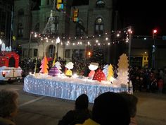 a parade float with christmas decorations and lights on the street in front of a large building