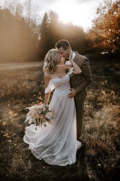 a bride and groom are standing in the grass with their arms around each other as they kiss