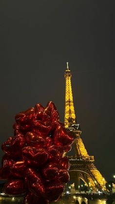 the eiffel tower lit up at night with red balloons in front of it