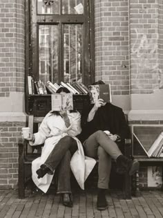 two people sitting on a bench with books in their hands and one person holding a book