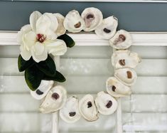 a wreath made out of seashells on a window sill with a white flower