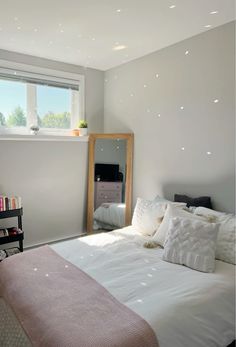 a bedroom with a bed, dresser and mirror in it's corner next to a window