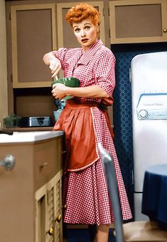 a woman in a red and white checkered dress is holding a green cup while standing next to an oven