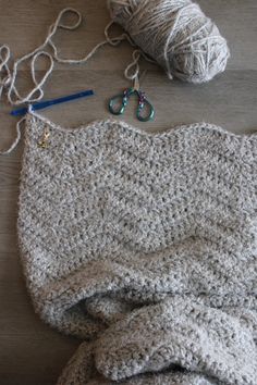 yarn and scissors are laying on the floor next to a crocheted blanket